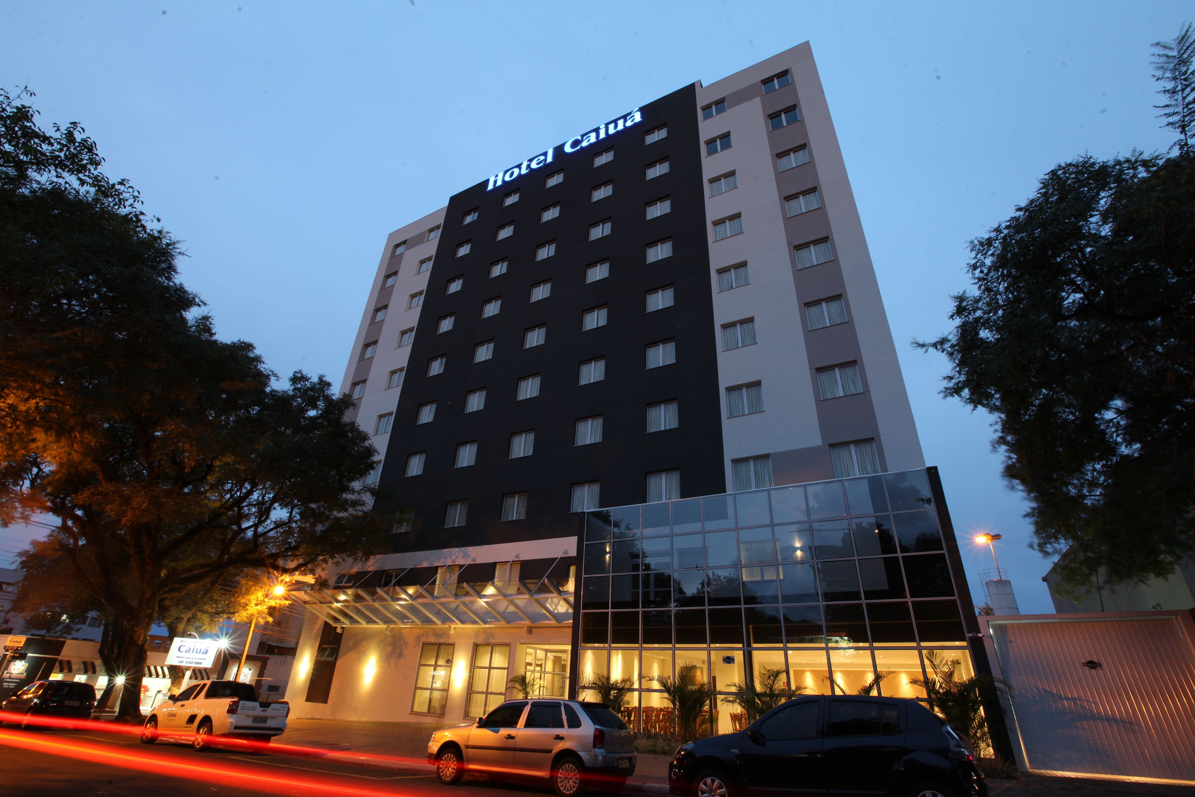 Um hotel com vários andares e fachada de vidro, com uma placa que diz 'Hotel Caia'.