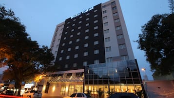 Um hotel com vários andares e fachada de vidro, com uma placa que diz 'Hotel Caia'.