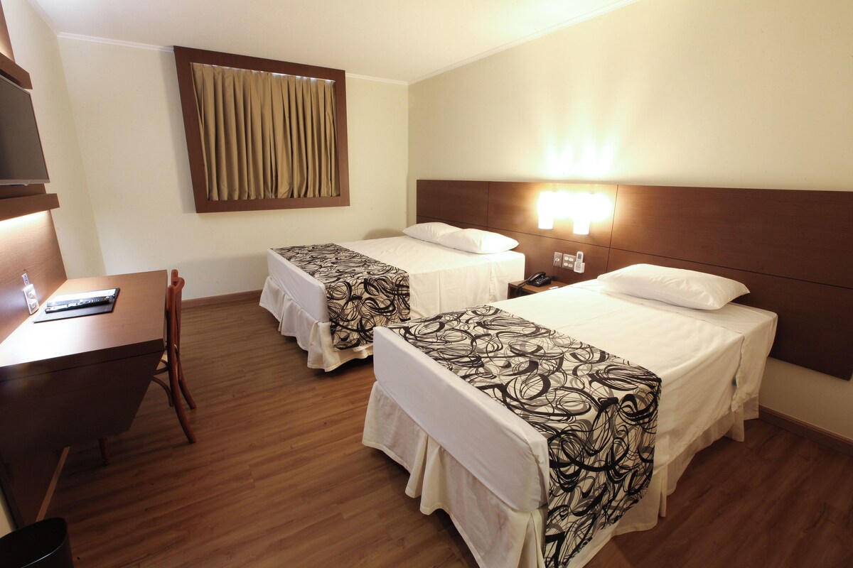 A hotel room with two beds, a desk, a chair, and a TV.