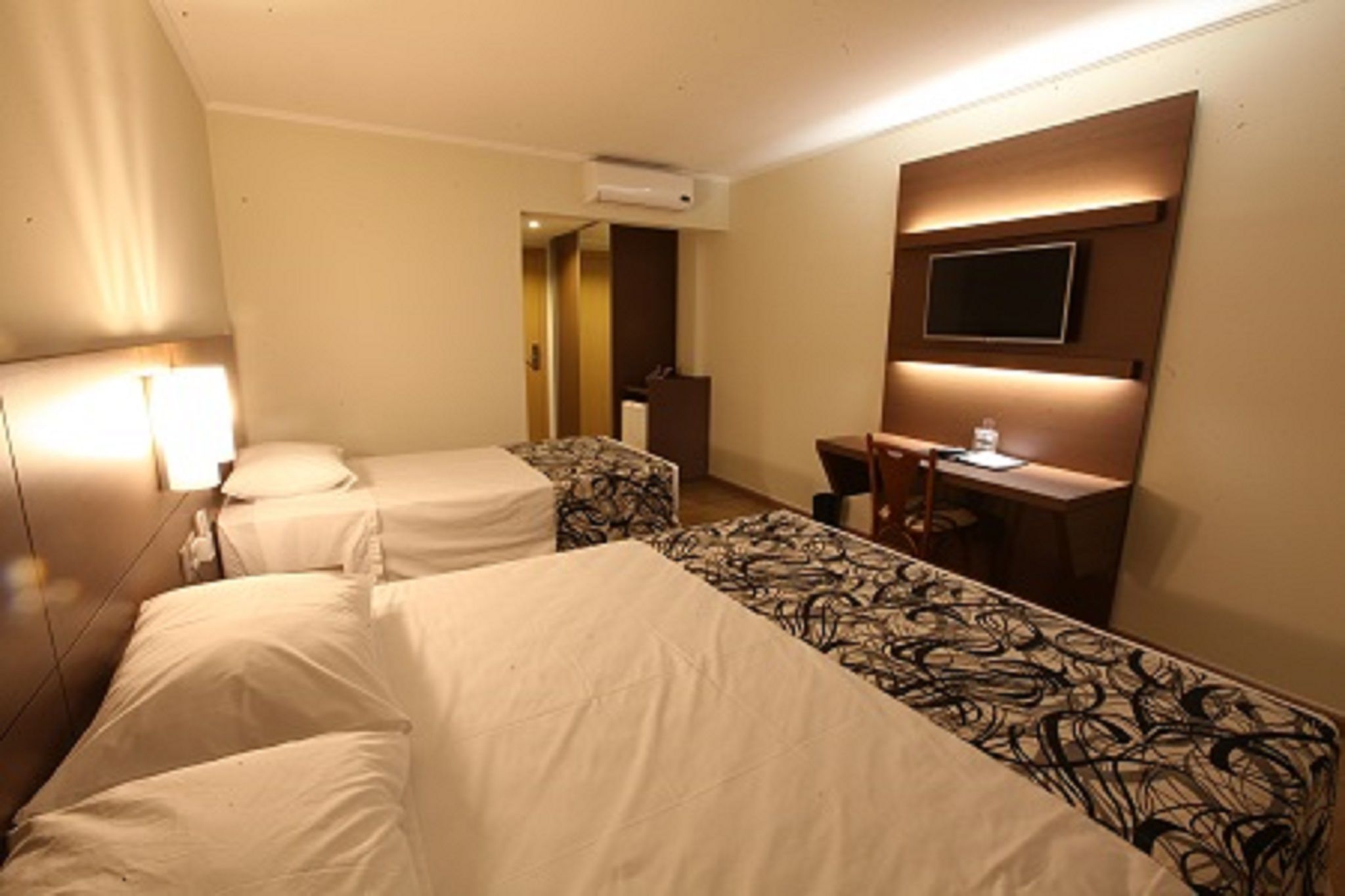 Habitación de hotel con dos camas, un escritorio, una silla, un televisor y un equipo de aire acondicionado.
