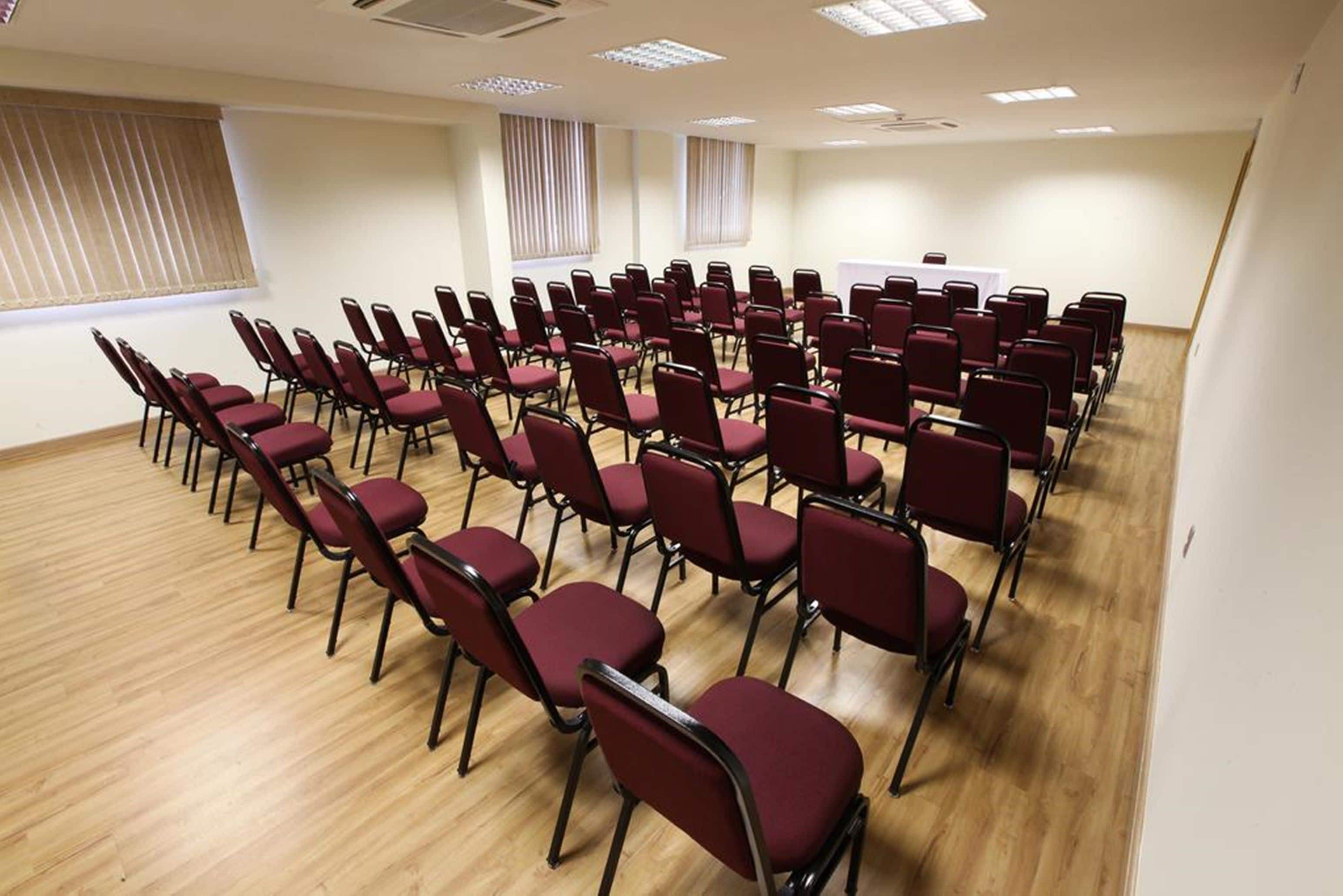 Un salón de conferencias con filas de sillas, una pizarra y ventanas con persianas.