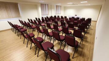 Un salón de conferencias con filas de sillas, una pizarra y ventanas con persianas.