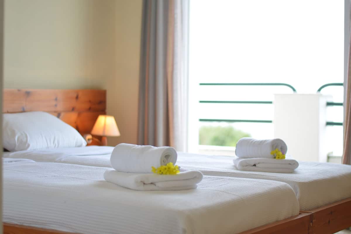 A hotel room with two beds, each with neatly folded white towels and a small yellow flower.