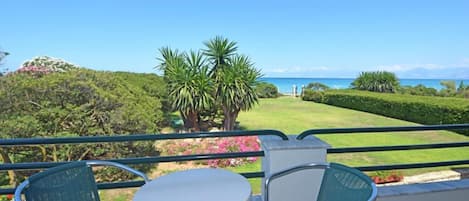 A balcony with a table and chairs, overlooking a well-manicured lawn and the ocean.