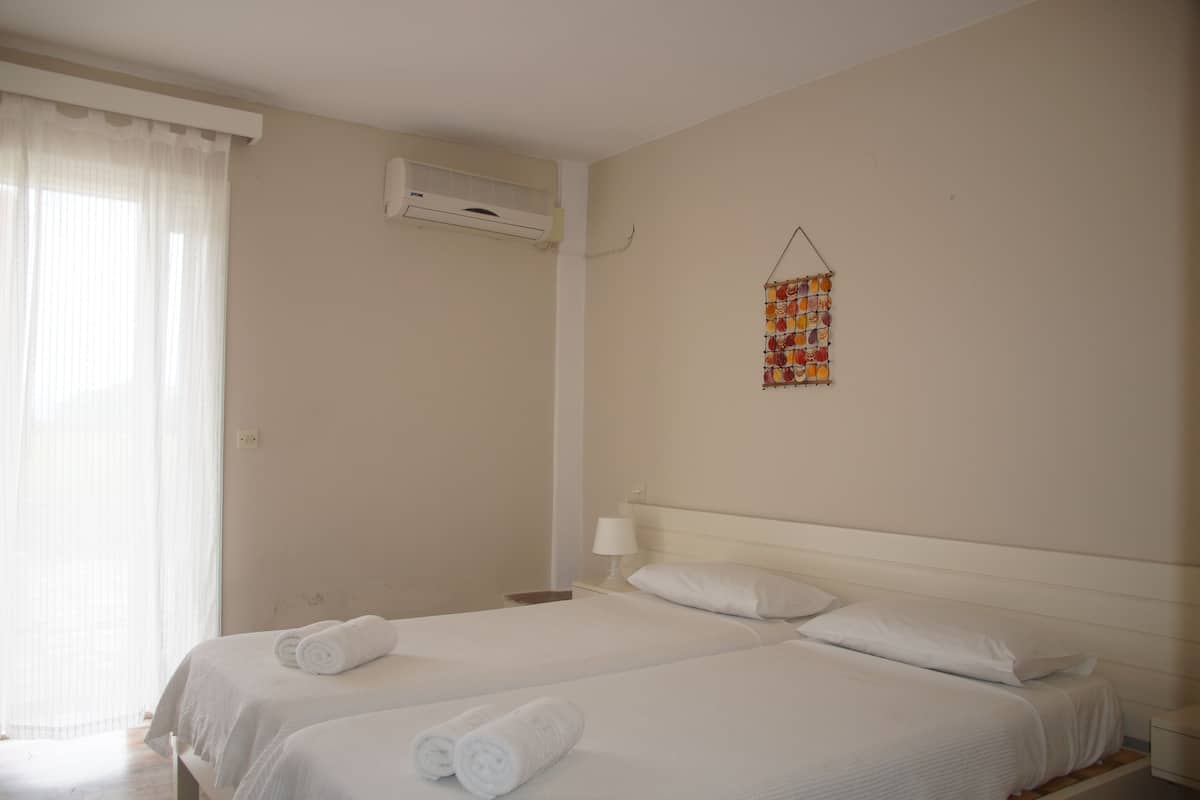 A hotel room with two beds, a window with sheer curtains, an air conditioning unit, and a wall-mounted decoration.
