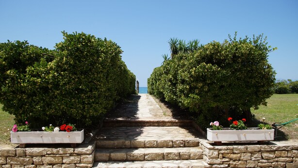 A stone pathway leading to a view, flanked by trimmed hedges and flower planters. - Akti Anastasia (Corfu)