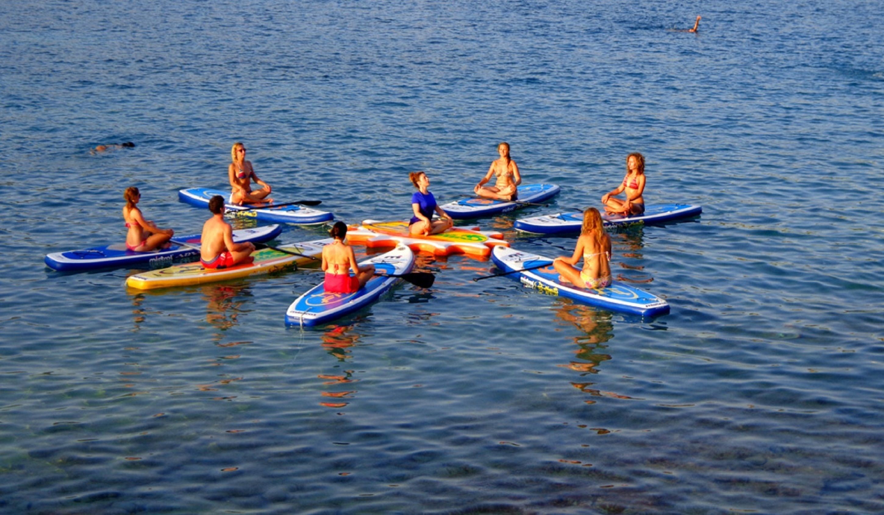 A group of people sitting on paddleboards in a calm body of water.