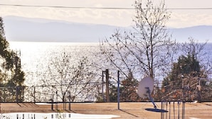 A table with a plaid tablecloth, a metal railing, and a view of a body of water with mountains in the background.