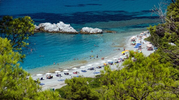 A beach with clear blue water, rocky formations, and people enjoying the sun.