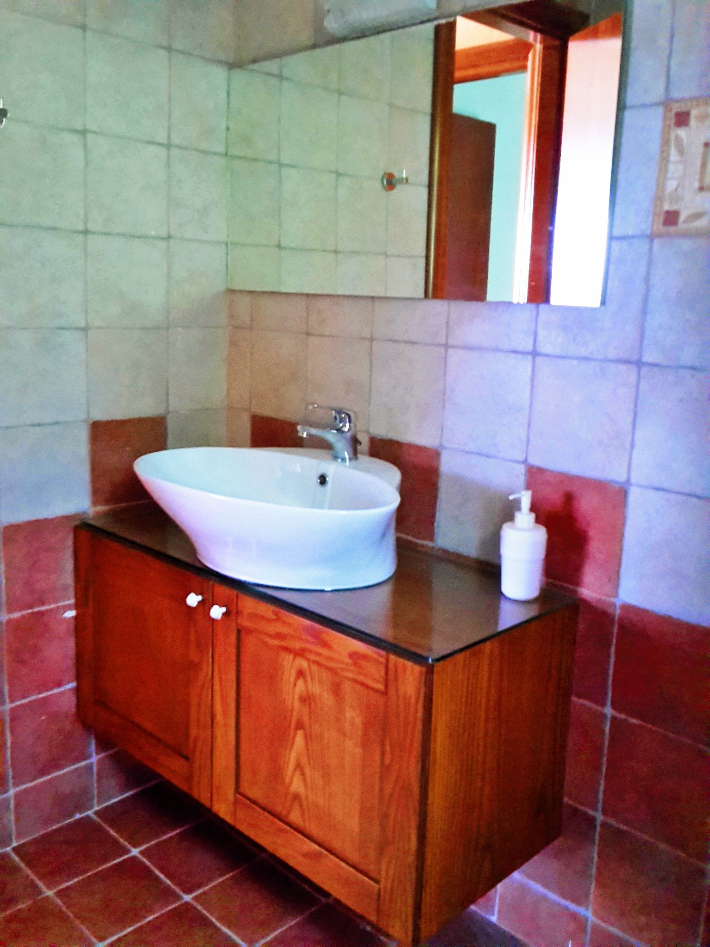 A bathroom with a white sink, wooden vanity, and red-tiled walls.