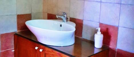 A bathroom with a white sink, wooden vanity, and red-tiled walls.