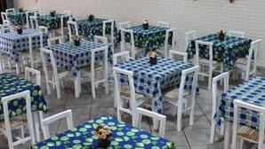 Varias mesas con sillas blancas, cada una cubierta con un mantel azul con estampado de hojas verdes.