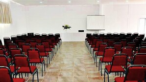 Un salón de conferencias con filas de sillas rojas, una pizarra y suelo de baldosas.