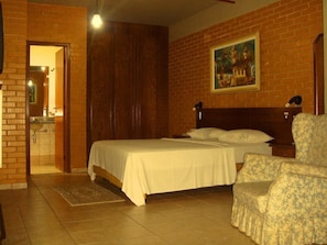 A bedroom with a bed, a chair, a painting on the wall, and a bathroom visible through an open door. - Rede Andrade Goiânia Centro (Goiânia)