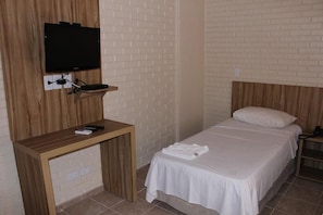Une chambre d’hôtel avec un lit, un téléviseur fixé sur un panneau en bois, une petite table en bois et une table de chevet.