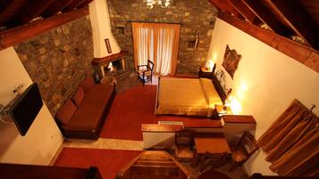 Un dormitorio acogedor en el ático con pared de piedra, chimenea, cama y escalera de madera.