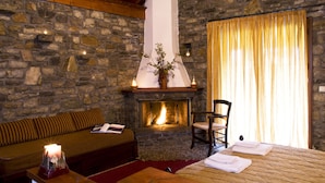 A cozy room with a stone fireplace, a sofa, a chair, and a bed with towels. - Ta Petrina (Nafpaktos)