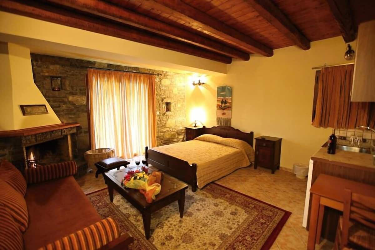 A cozy room with a fireplace, a bed, a small table with flowers, and a stone wall.