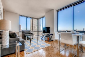 A modern living room with a sofa, a coffee table, a TV, and a dining area with chairs and a table.