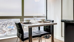 A dining area with a table set for two, a city view through large windows, and a modern floor lamp. - Global Luxury Suites at Columbus (Jersey City)