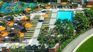 A rooftop pool area with multiple lounge chairs and umbrellas, surrounded by greenery and a clear blue pool. - Global Luxury Suites at Columbus (Jersey City)