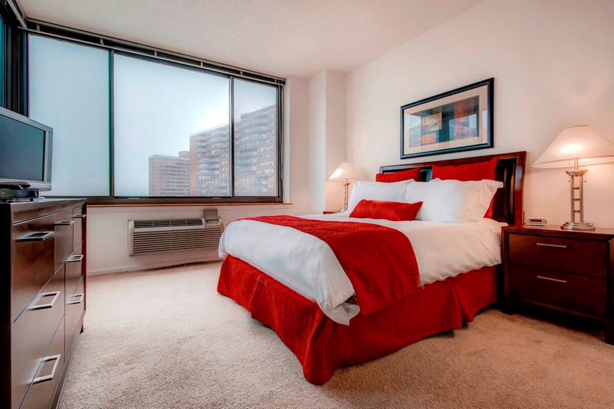 Une chambre d’hôtel moderne dotée d’un grand lit, d’une télévision, d’un radiateur et d’une fenêtre donnant sur la ville.