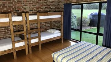Une pièce avec trois lits superposés et un lit simple, des murs en briques et une grande fenêtre donnant sur un paysage verdoyant.