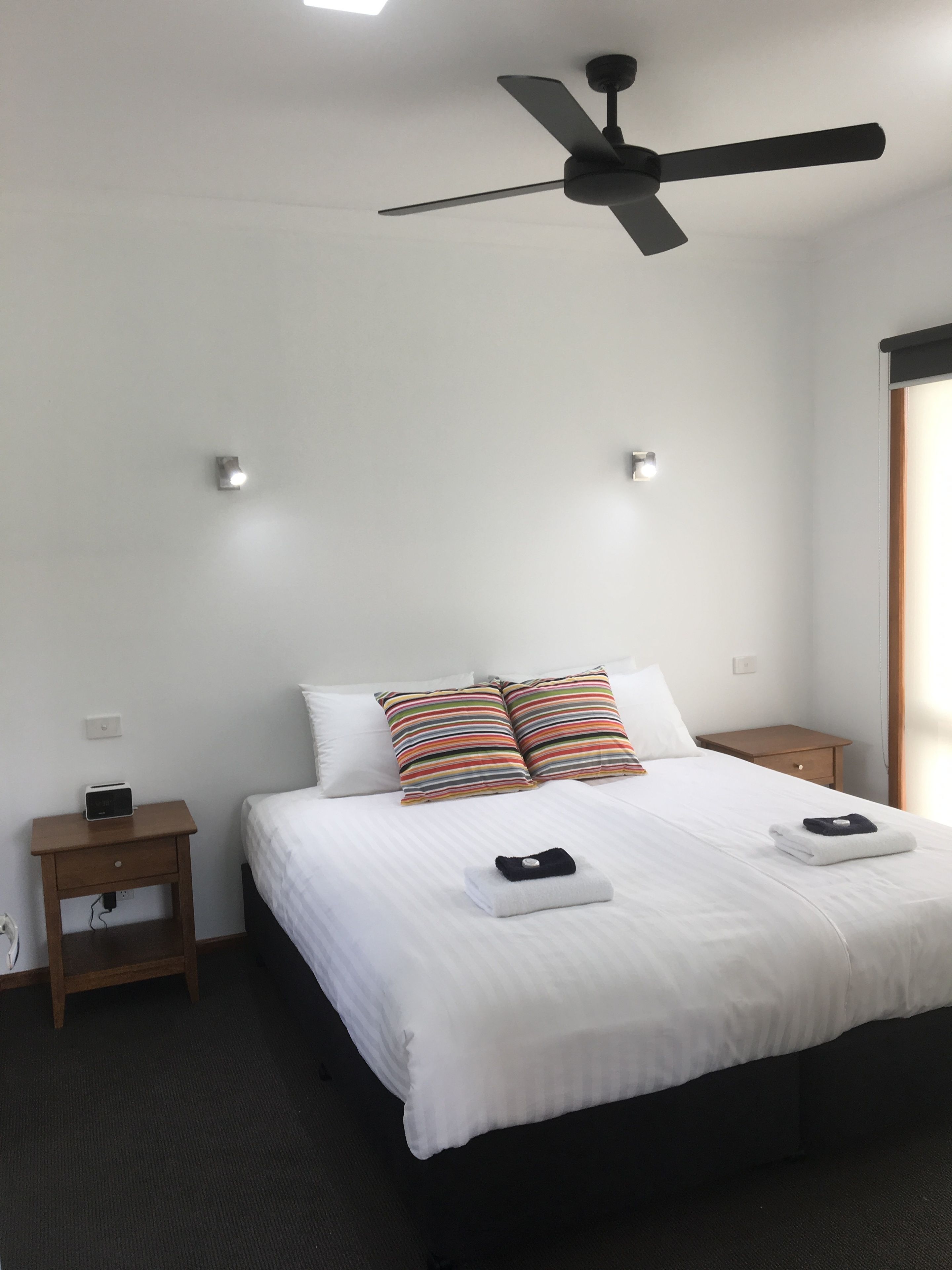 A hotel room with a bed, two bedside tables, a ceiling fan, and a window with curtains.