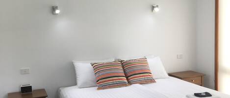 A hotel room with a bed, two bedside tables, a ceiling fan, and a window with curtains.