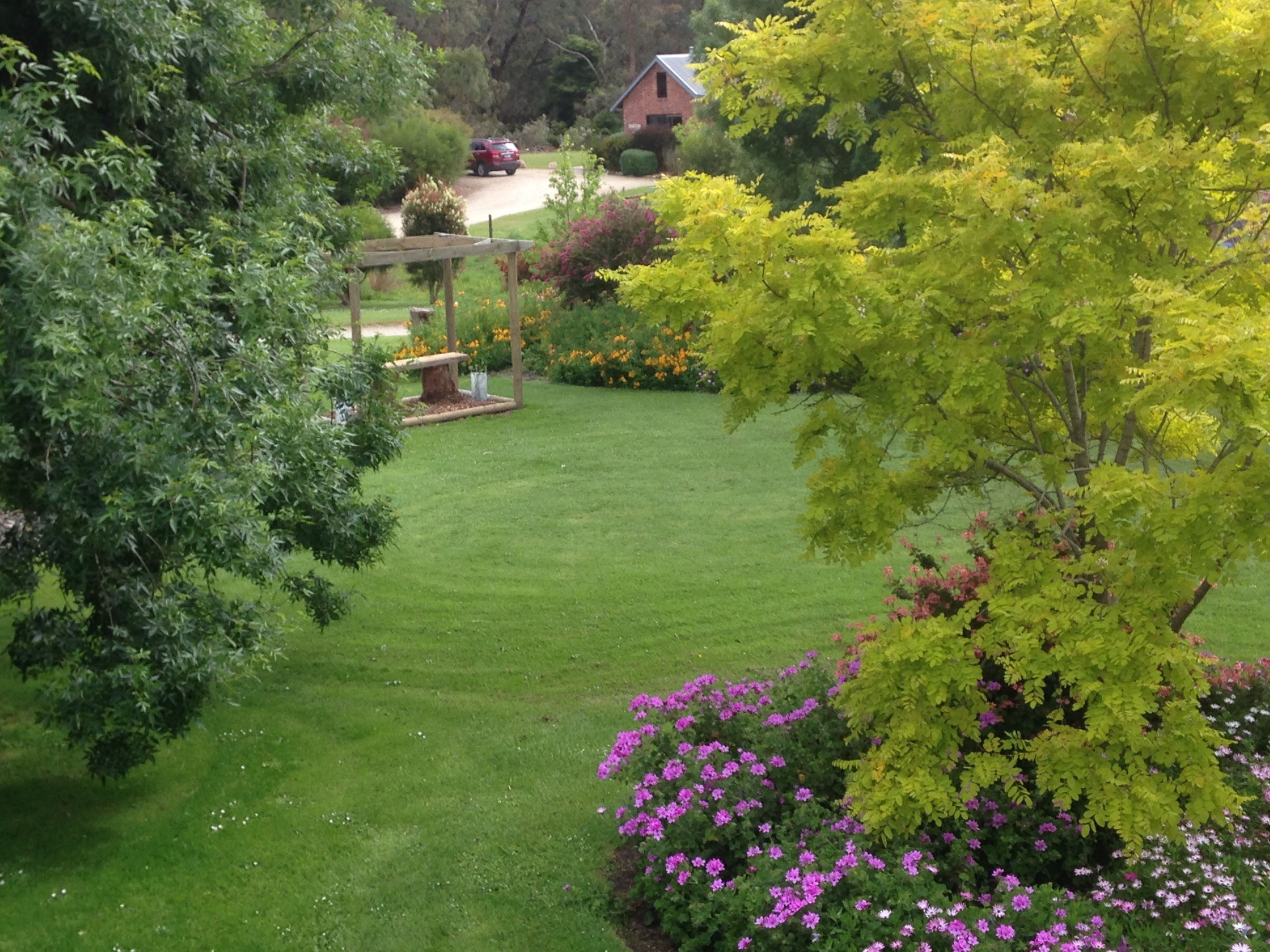 A well-maintained garden with a lawn, a wooden pergola, and flowering plants.