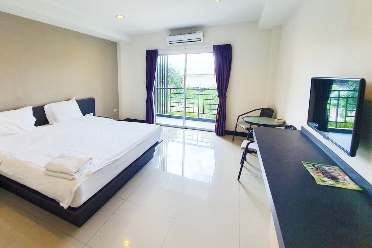 Quarto de hotel com uma cama grande, uma mesa com cadeira, televisão e janela com cortinas.
