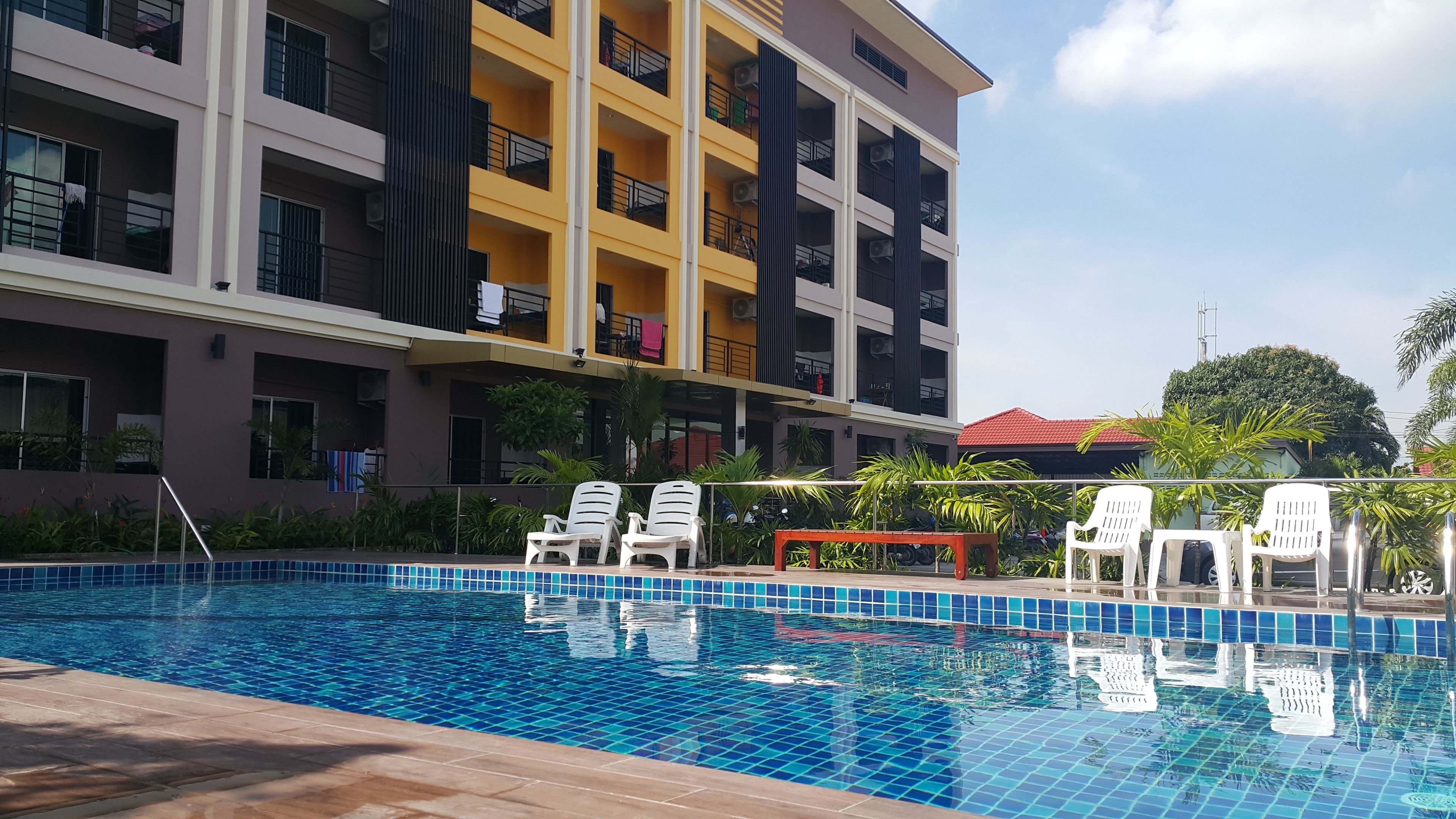 A swimming pool with tiled blue and white patterns, surrounded by white lounge chairs and a red bench.