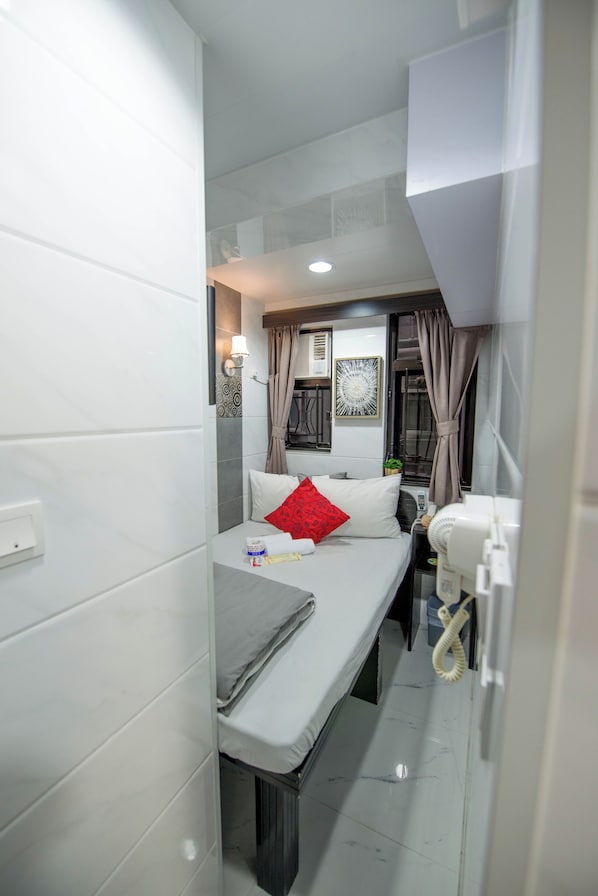Habitación de hotel pequeña con una cama individual, una mesita de noche, un escritorio pequeño y una ventana con cortinas.