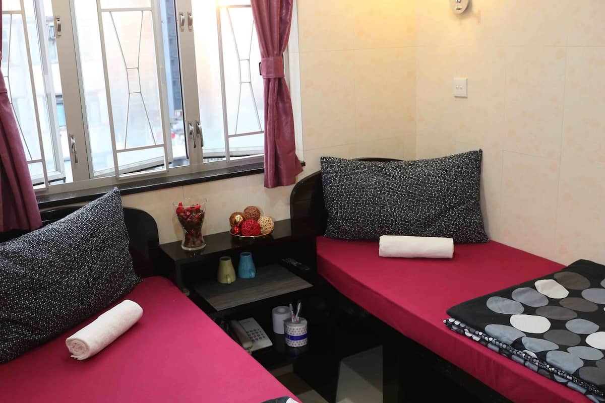 Une chambre avec deux lits, chacun recouvert d’une couvre-lit à pois, une petite table avec un vase de fleurs et une fenêtre avec des rideaux.