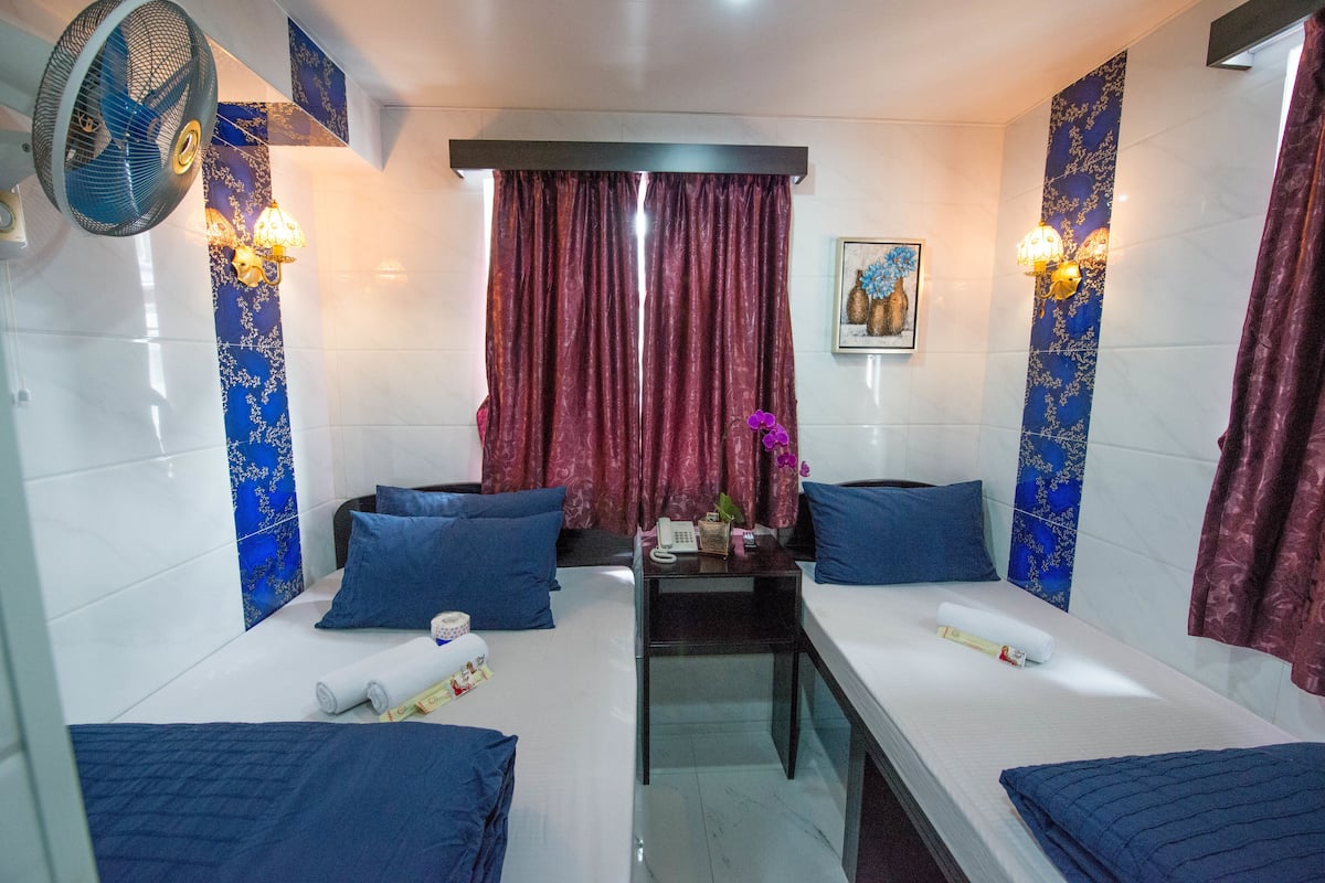 Une chambre d’hôtel avec deux lits, une petite table, un ventilateur et des panneaux décoratifs sur les murs.