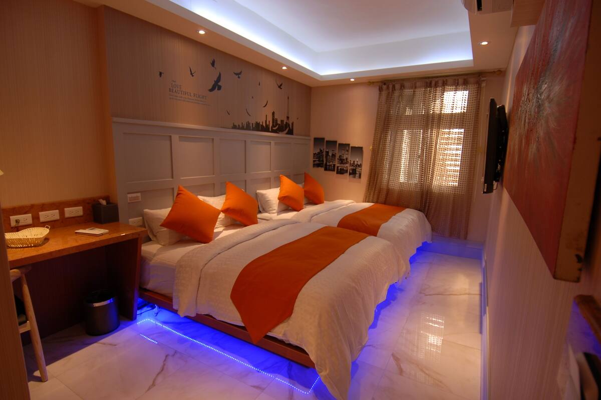 A bedroom with a large bed, a desk, and a wall with artwork.