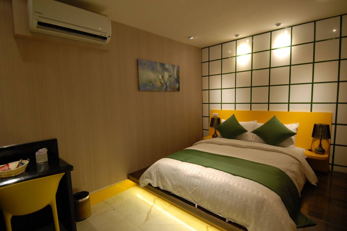 A hotel room with a bed, bedside table, lamp, and artwork on the wall.