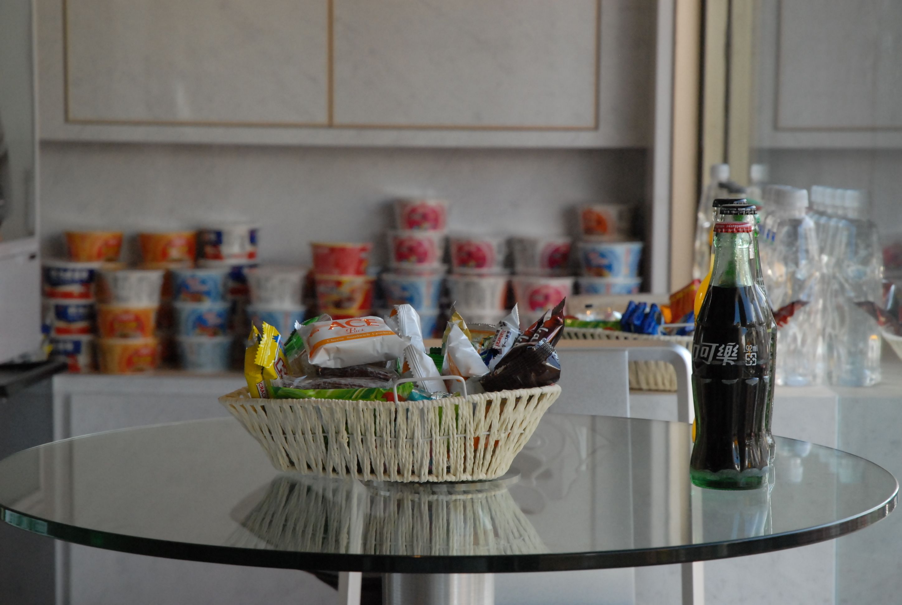 A kitchen with a glass table holding a basket of snacks and a bottle of soda.