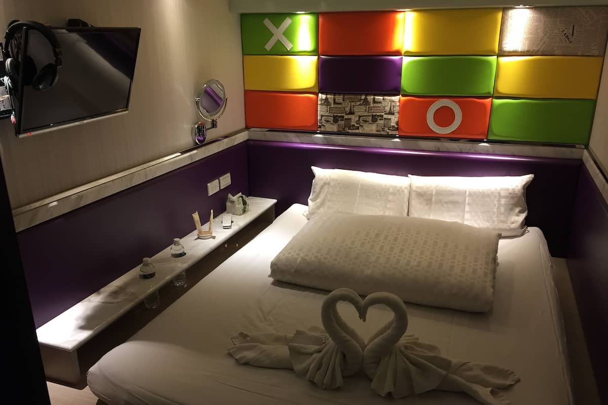 A hotel room with a bed, a bedside table, a TV, and a colorful wall panel.