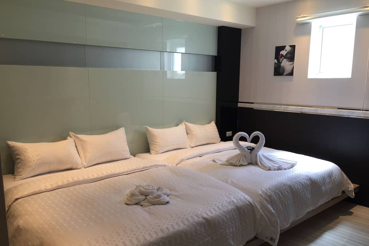 A hotel room with two beds, each with white linens and pillows. There are two swan-shaped towels on the beds. The room has a modern design with a large mirror above the beds and a picture on the wall.