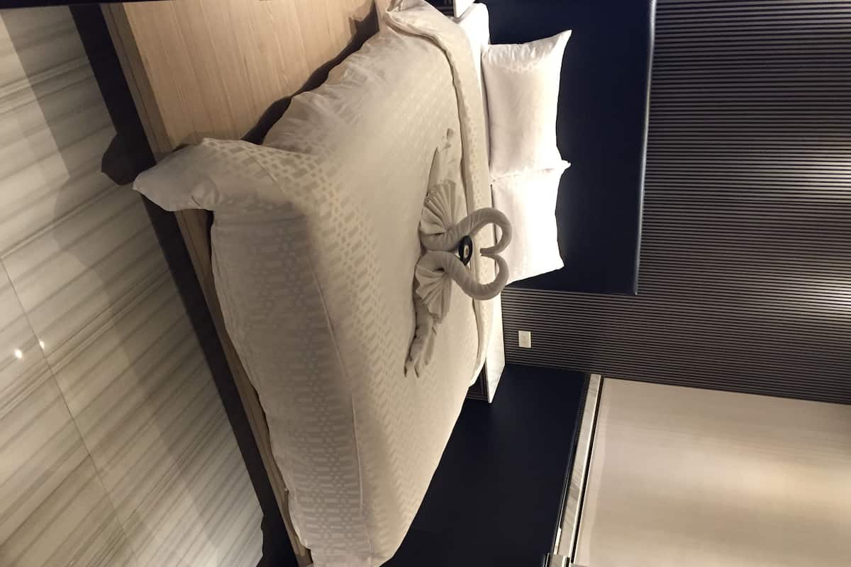 A bed with a white bedspread and pillows, a dark headboard, and a visible power outlet.