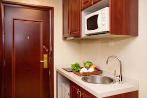 Cocina compacta con microondas, fregadero y una cesta de verduras en la encimera.