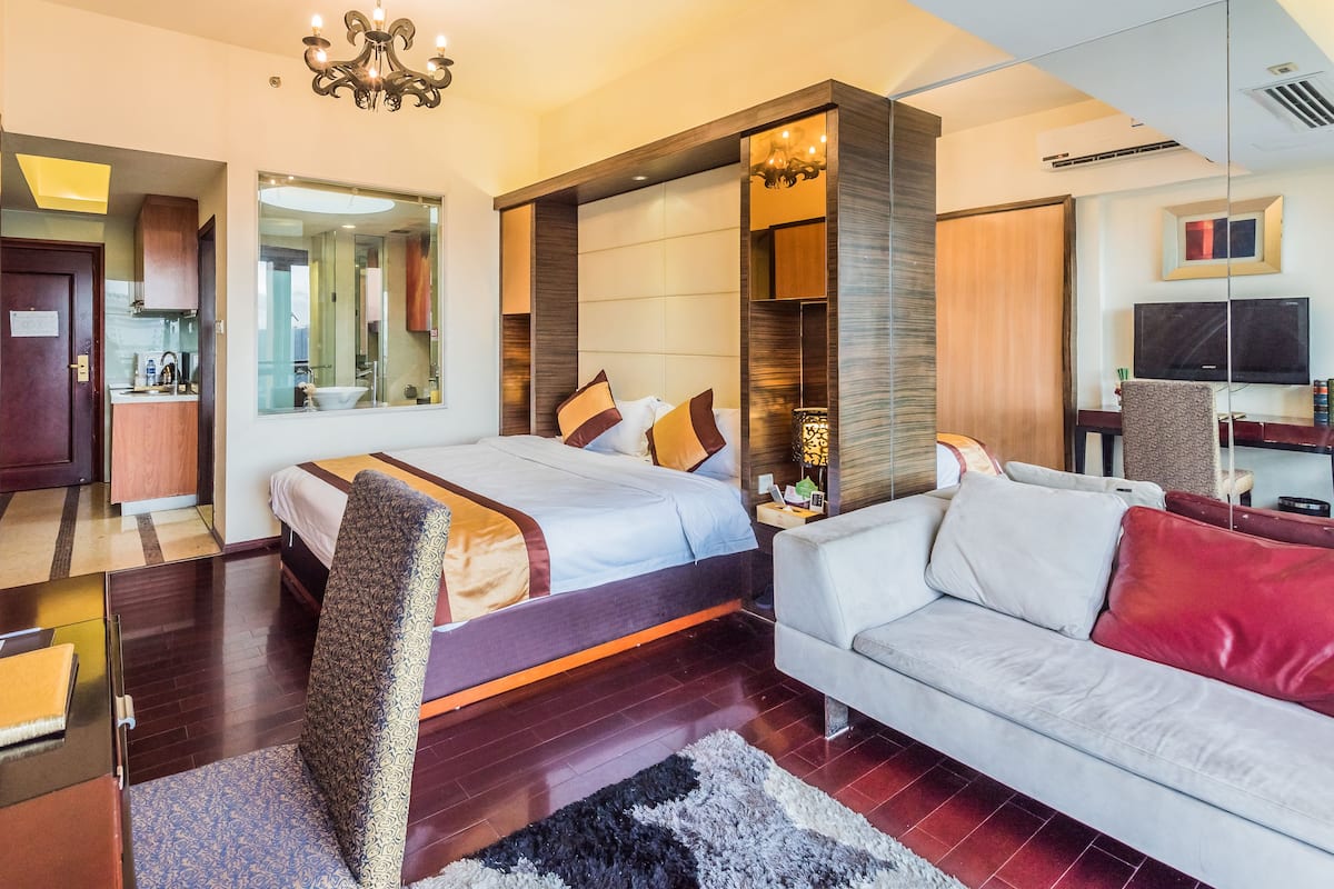 Een moderne hotelkamer met een groot bed, een bank, een bureau en een badkamer die door een geopende deur zichtbaar is.