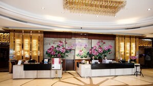 Un hall d’accueil d’hôtel avec deux comptoirs de réception, un grand tableau représentant des fleurs et un lustre moderne.