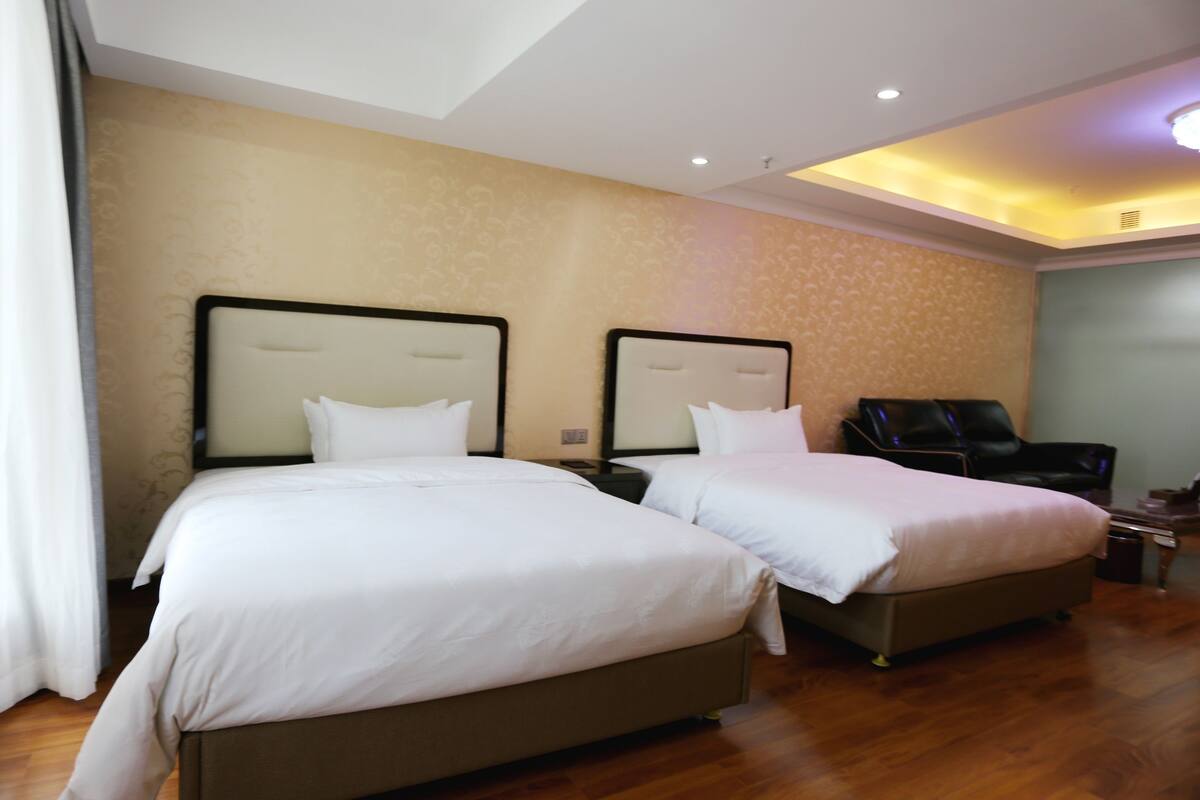 Habitación de hotel con dos camas, una zona de estar e iluminación en el techo.