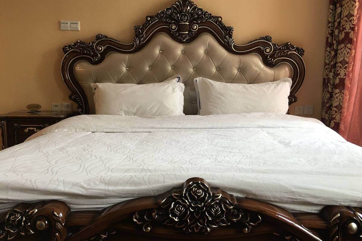 Una cama con cabecera tapizada, dos almohadas y estructura de madera con adornos florales.