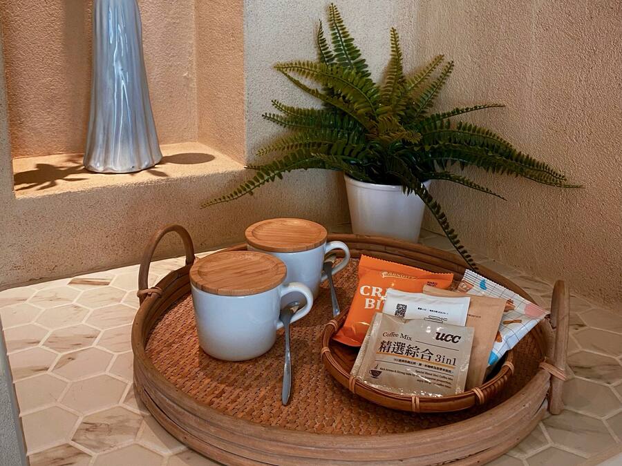 Een dienblad met twee witte bekers, een lepel en een zakje koffiemelk op een vloer van honingraatmozaïek.