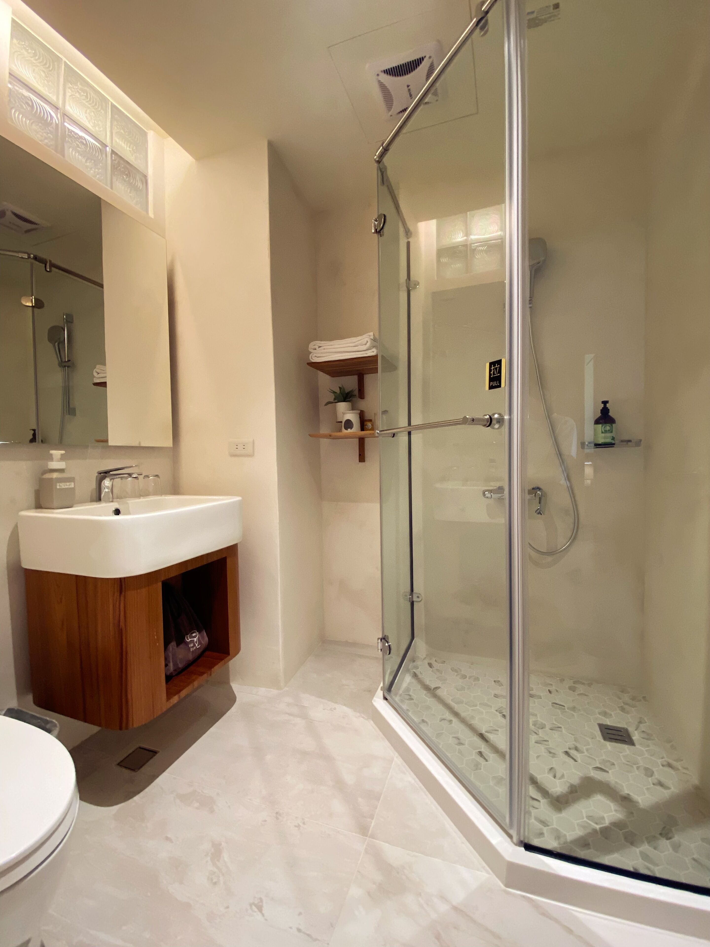 A modern bathroom with a glass-enclosed shower, a wooden vanity, and a large mirror.