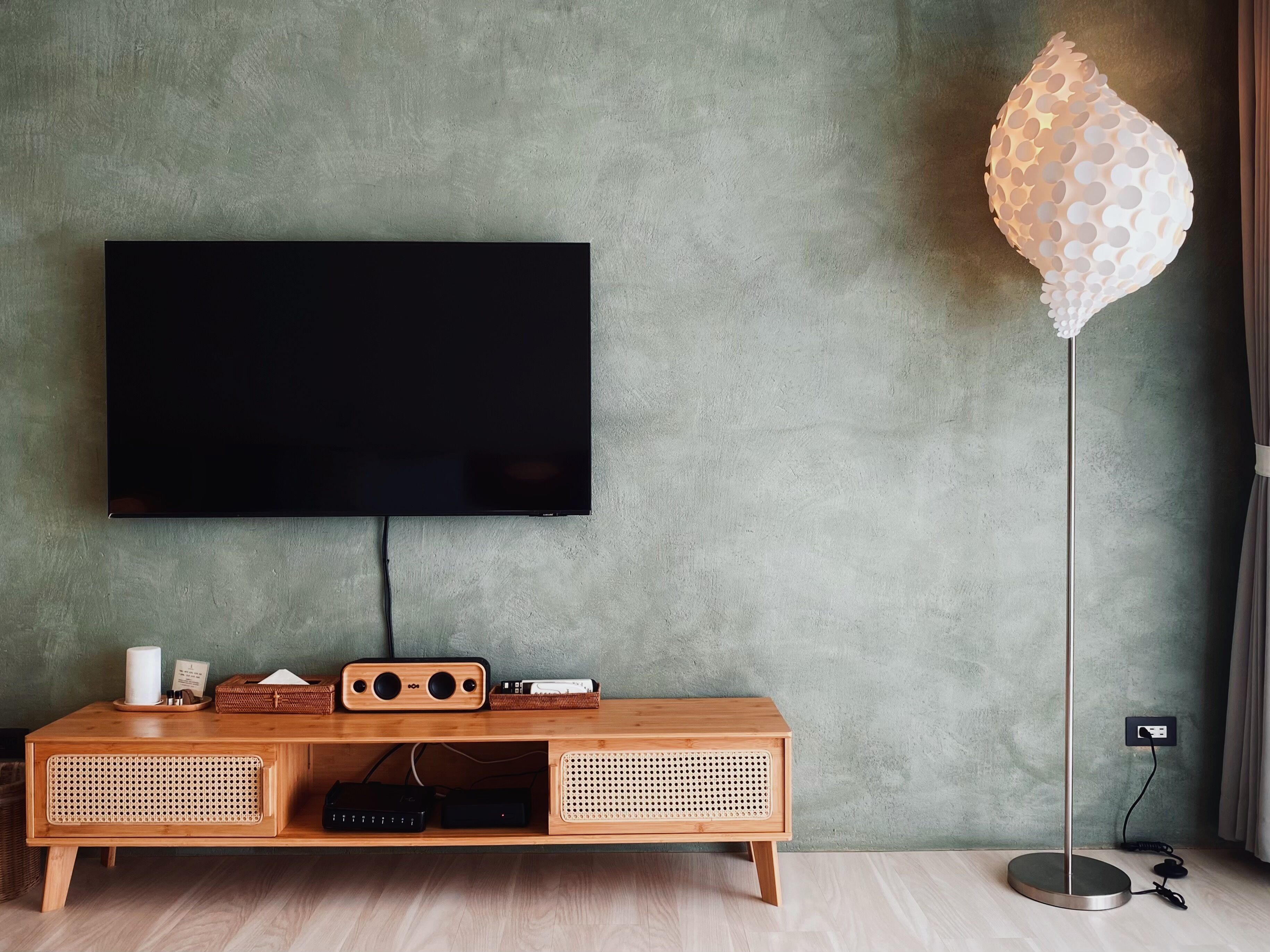 A modern living room with a flat-screen TV mounted on a textured wall, a wooden console table with speakers and a remote, and a unique spherical floor lamp.