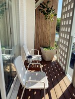 A balcony with two white metal chairs, a table, a potted plant, and a bamboo screen.
